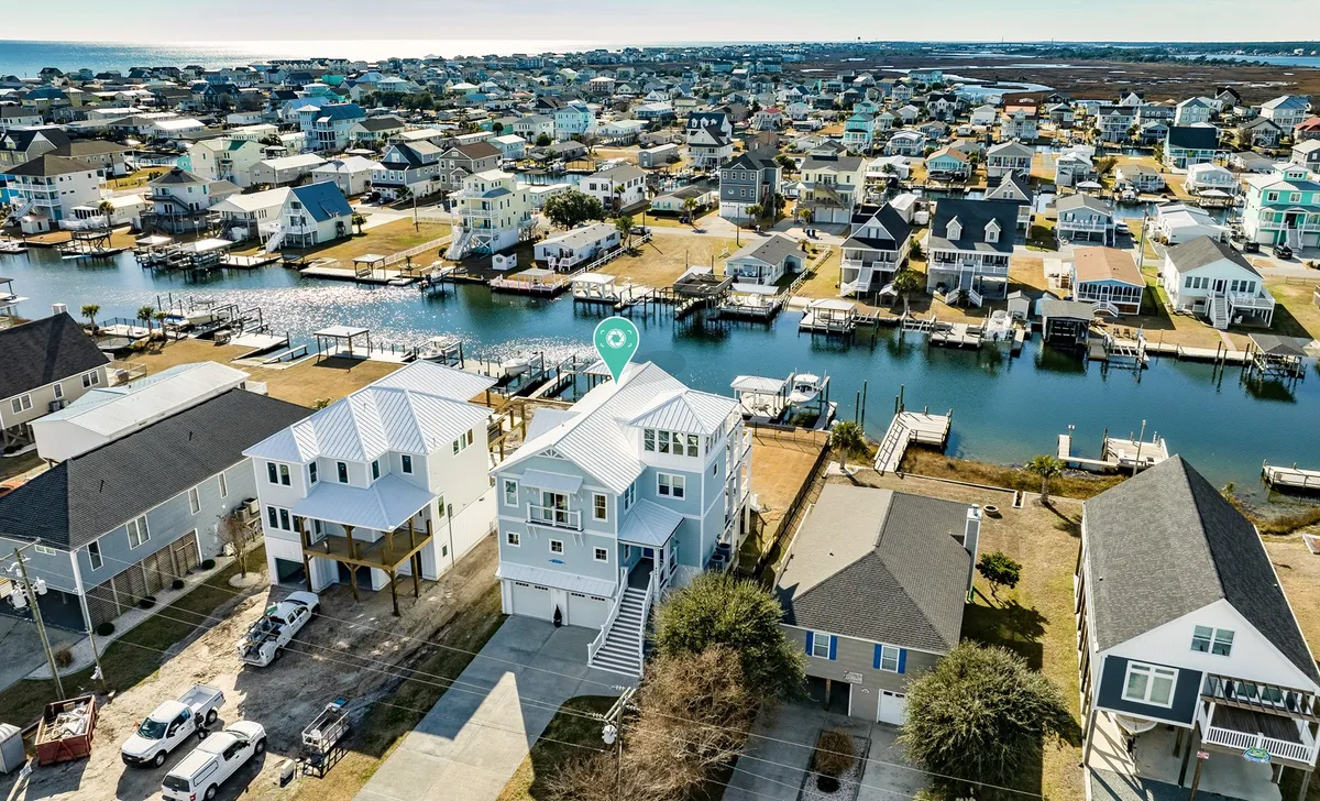 A stunning exterior view of a waterfront house showcases its proximity to the marina and canal, with ample outdoor space for boating, fishing, and family gatherings. The surrounding water and dock reinforce the theme of upscale island living and exploration.