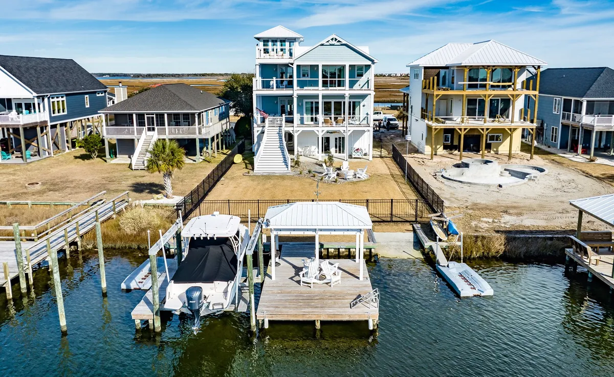 A vibrant waterfront view featuring a multi-story house, several docks with boats, and lively outdoor spaces. The scene captures people sunbathing, gathering for family activities, and preparing for fun on the water.