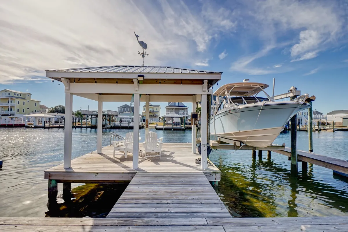 A tranquil wooden dock extends over the water, complete with a boat, a small seating area, and a classic weather vane. The atmosphere is peaceful, ideal for fishing, kayaking, or simply basking in sunrise or sunset views.