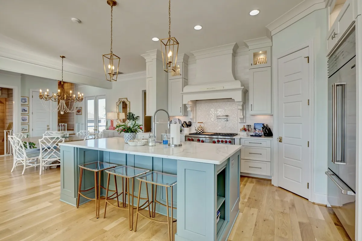 A stylish, modern kitchen with a central island and bar stools, pendant chandelier, high-end appliances, and a decorative tile backsplash. The open layout and inviting mood are perfect for cooking, entertaining, and hosting memorable meals.
