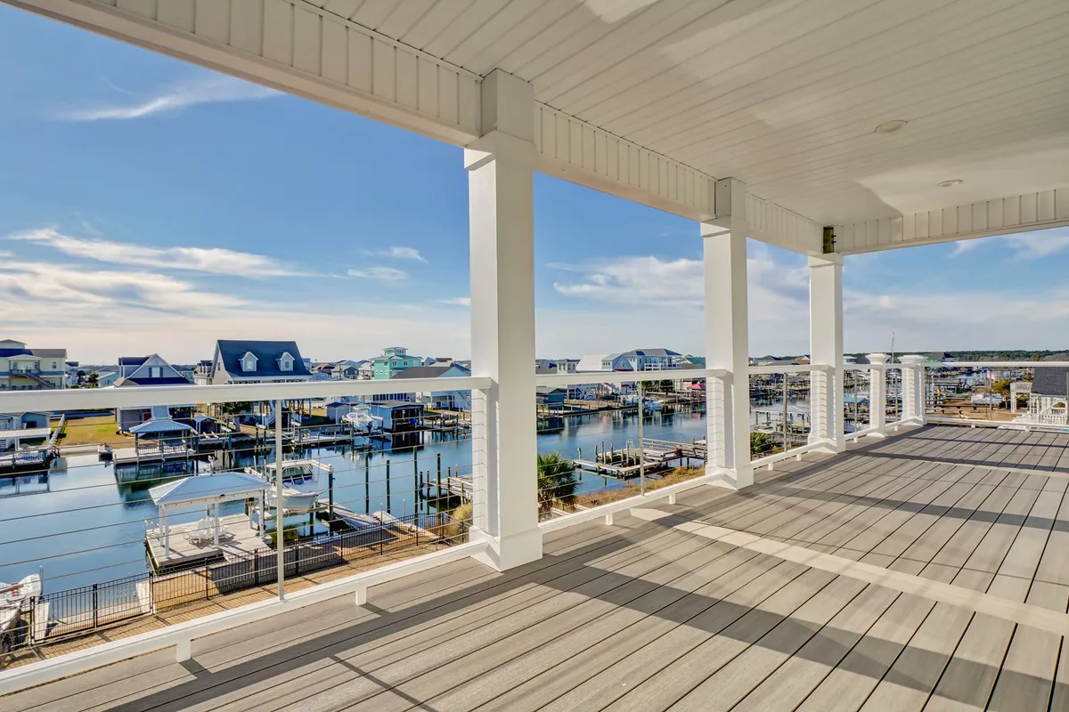 The image shows a spacious deck overlooking a tranquil marina, with boats gently floating by under a clear blue sky. Comfortable seating invites guests to relax outdoors, while the waterfront setting promises peaceful sunrises and memorable gatherings.