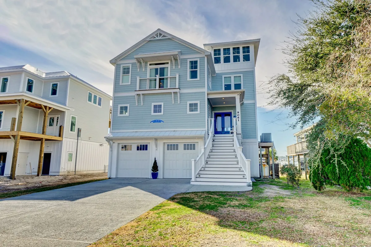 The exterior of a charming coastal home with inviting front steps, a striking blue door, and elegant architectural details. The scene is sunlit and cheerful, evoking a sense of welcome and anticipation for local adventures or relaxing after a day of exploration.