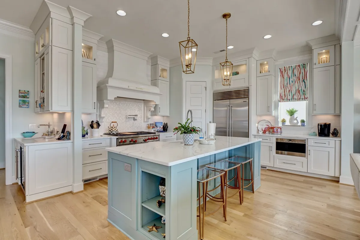 This image features a bright, contemporary kitchen with a spacious island, stainless steel appliances, and modern decorative lighting fixtures. The kitchen feels open and inviting, ideal for preparing meals, entertaining guests, and family gatherings.