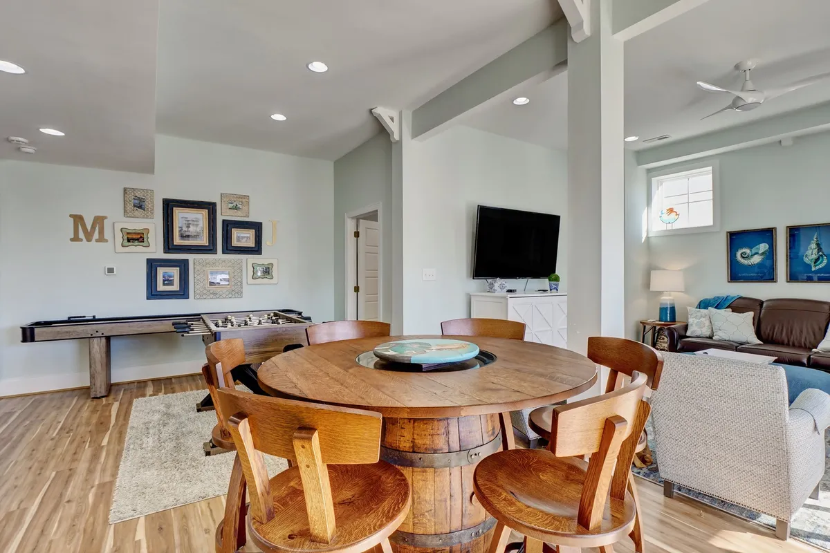 Here we see a welcoming entertainment space with a round wooden dining table, a sleek slate shuffleboard table, and a comfortable seating area complemented by framed artwork. The room exudes a relaxed, celebratory vibe—perfect for hosting game nights, casual gatherings, or milestone events.