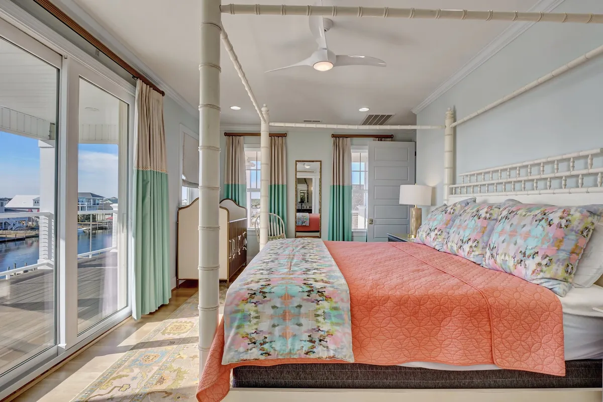 A tranquil bedroom featuring a canopy bed with colorful bedding, large windows that let in abundant natural light, and mirrored decor that adds a touch of elegance. The peaceful atmosphere and cozy textures invite relaxation and comfort.