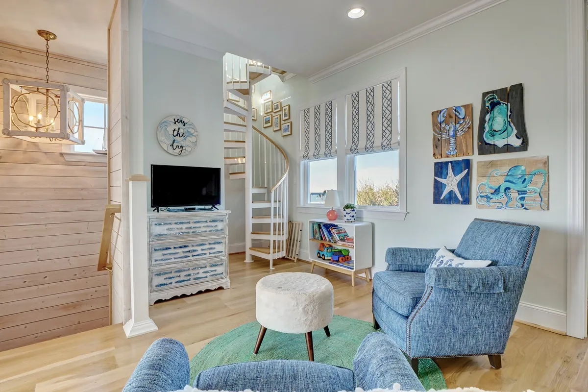 A cozy interior space featuring a spiral staircase leading upwards, artfully decorated walls, a comfortable armchair, and a decorative table. The area feels inviting, perfect for quiet moments or heading up to a special retreat space.
