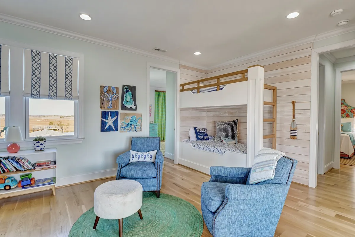 A playful, open bunk-bed room designed with children in mind, featuring bunk beds, a cozy reading nook, colorful wall art, and a comfy seating area. The space feels both fun and inviting, ideal for games, movies, and relaxation.