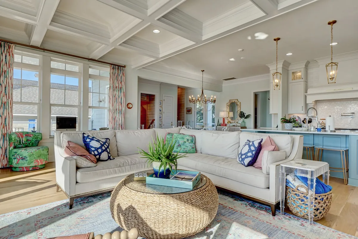 A brightly lit, welcoming living space is captured here, featuring a large sectional sofa, round coffee table, colorful armchairs, and a view into the kitchen area. The living room is designed for socializing, relaxing, and enjoying family moments, with ample seating and an airy feel.